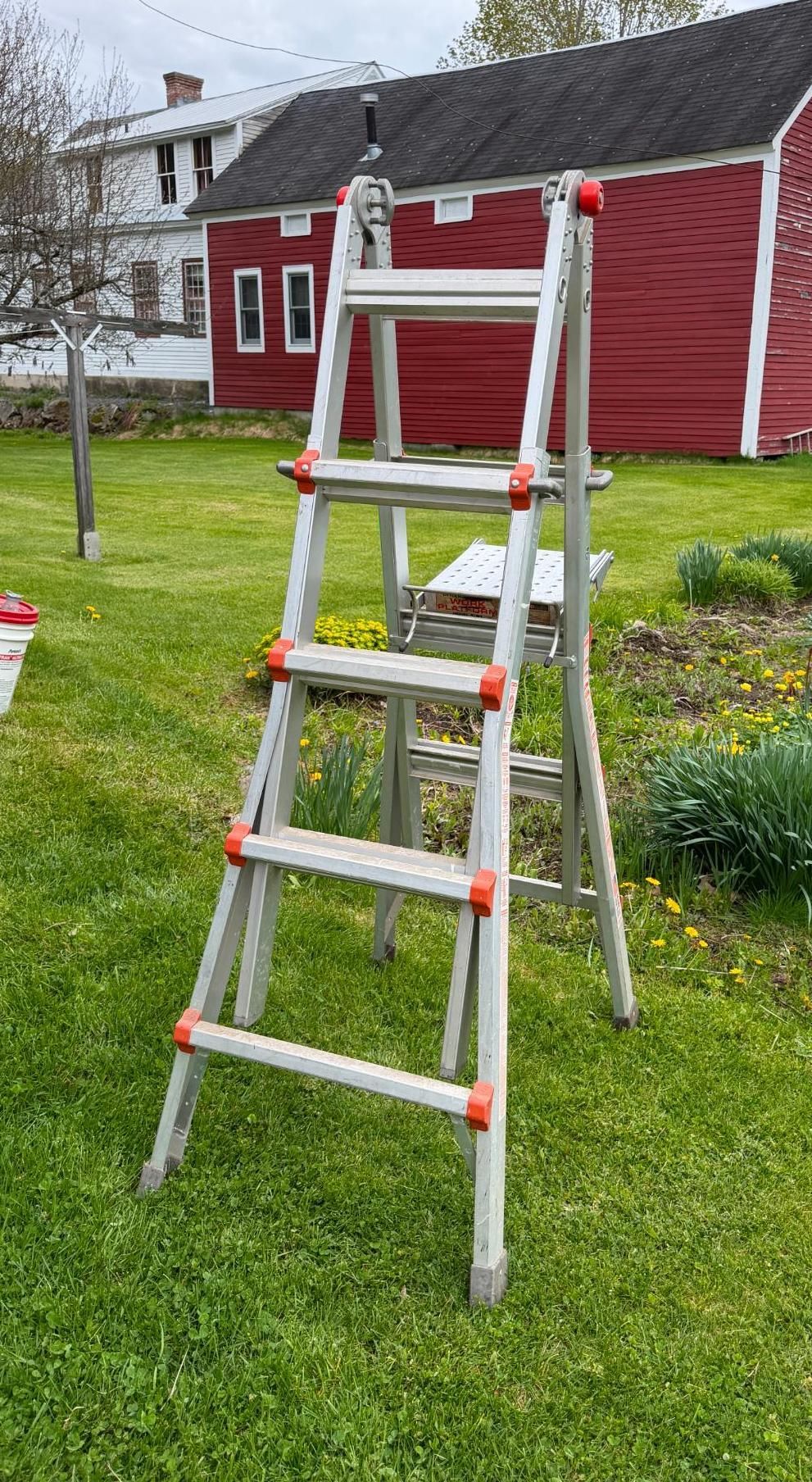 A white step ladder stands on a grassy lawn in front of a red house with white trim.