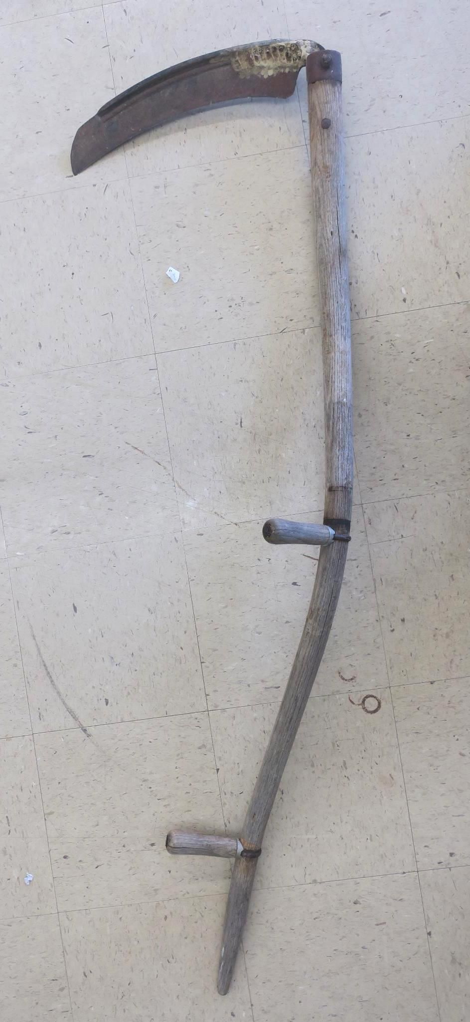 Old metal sickle with a curved blade and two short side prongs on a plain beige background