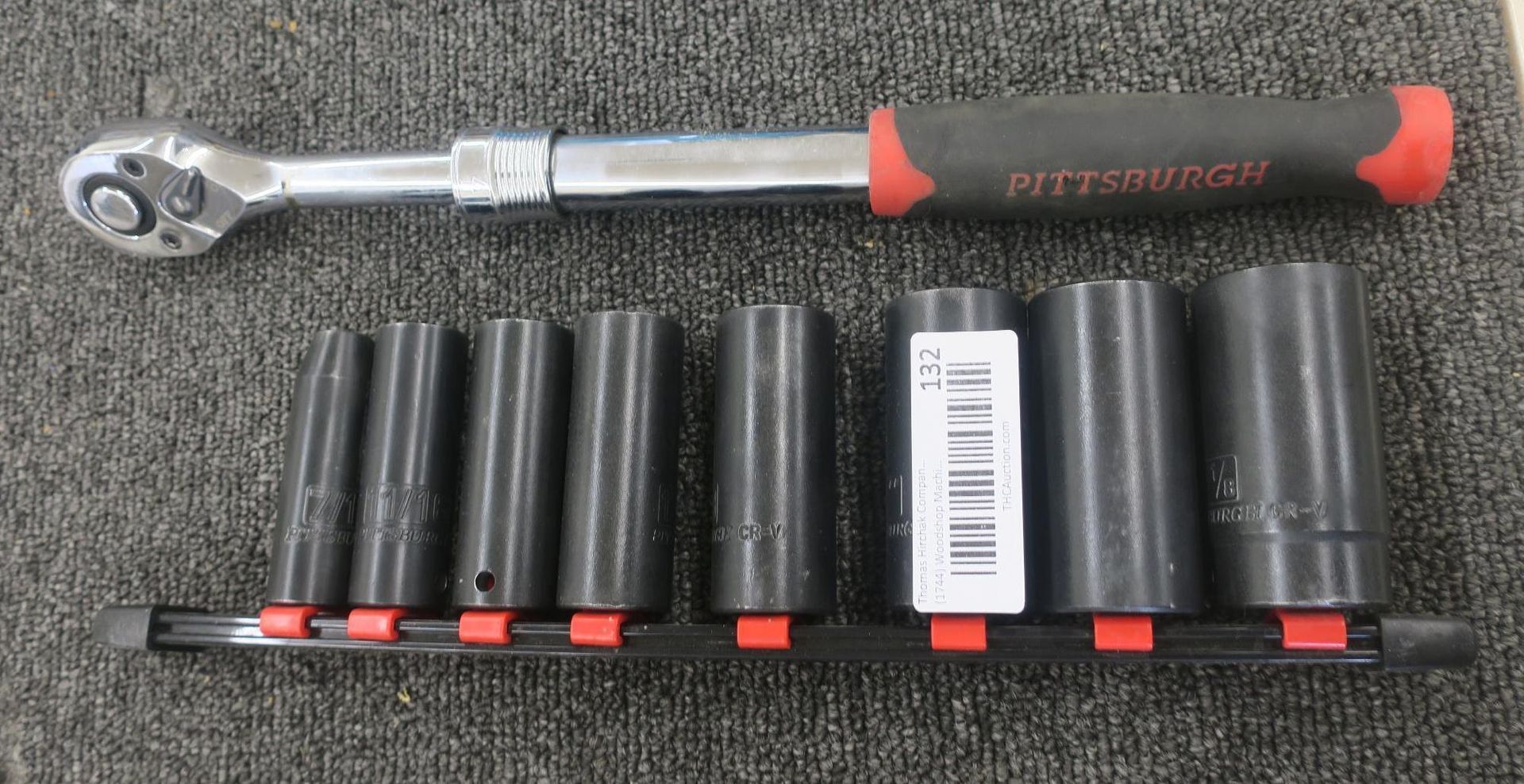 Chrome ratchet wrench above a set of black socket tools on a gray mat.