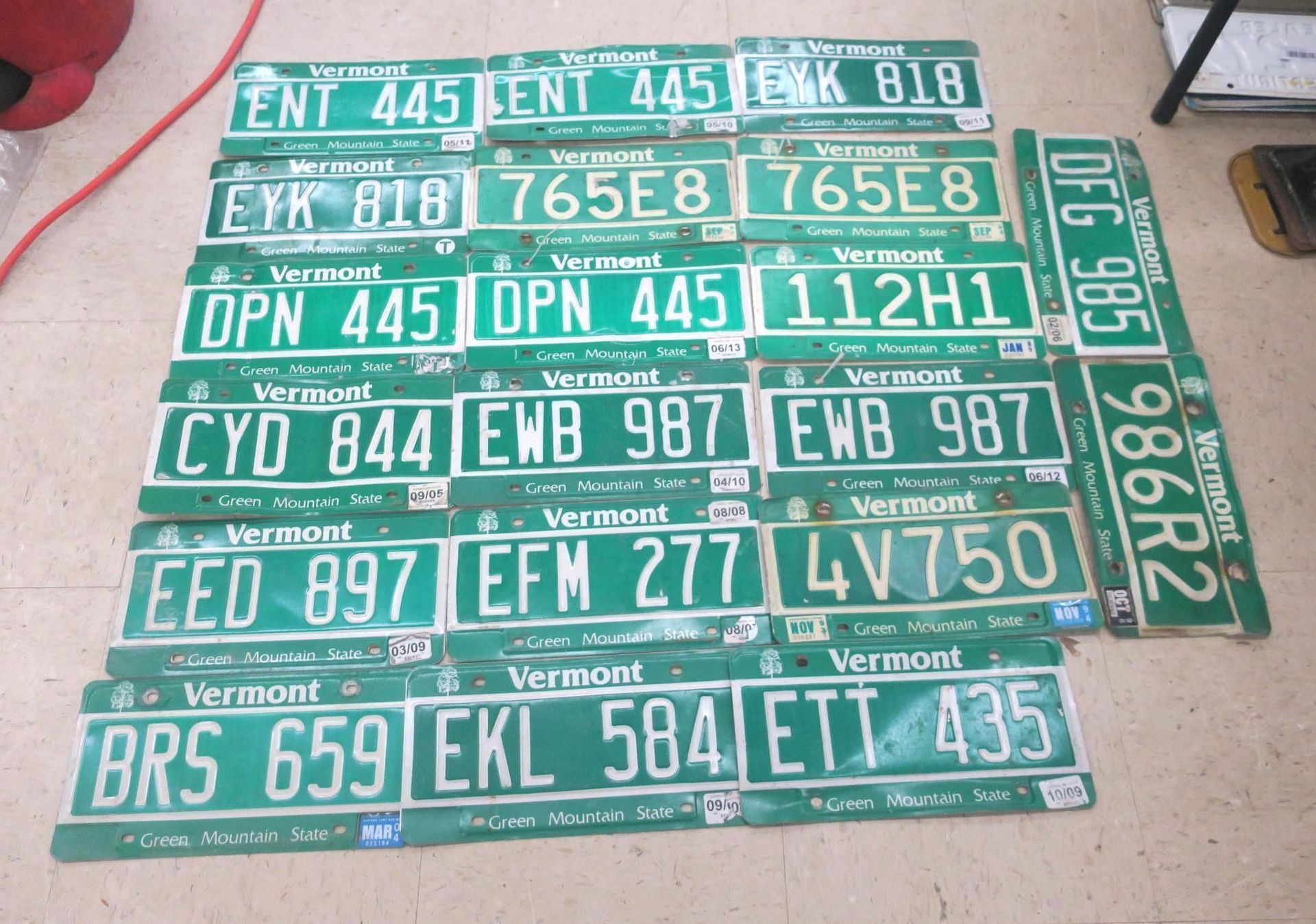 Stack of green Vermont license plates with white lettering, arranged in rows on a surface.