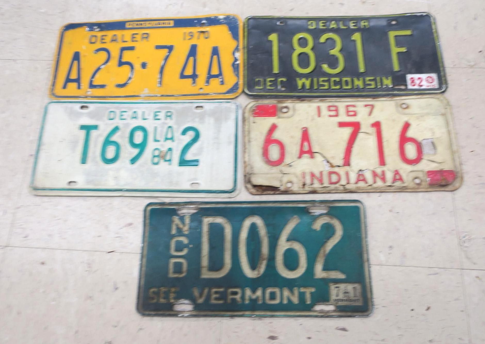Five vintage U.S. license plates arranged on a light surface, in yellow, white, red, and green.