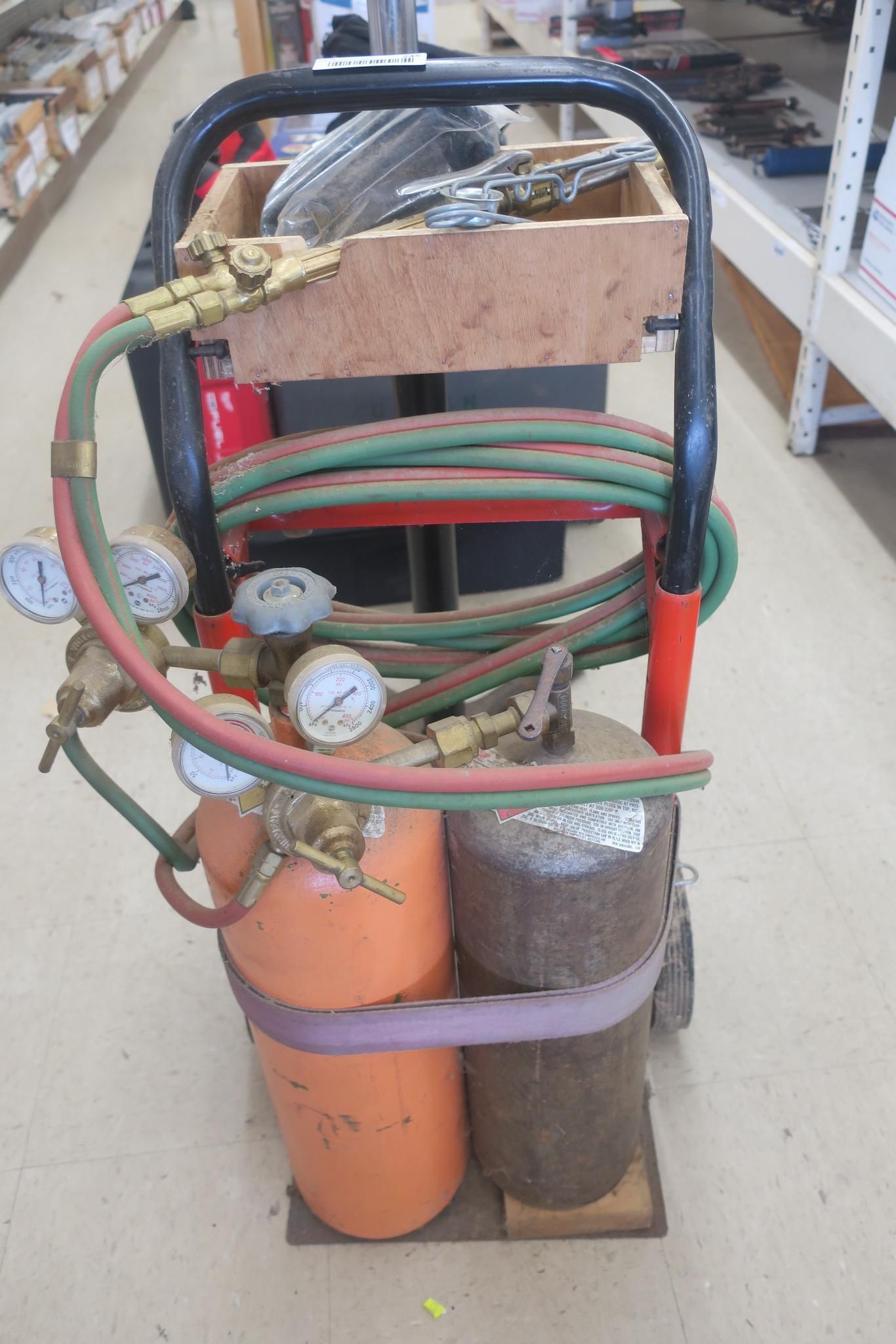 Gas cylinders strapped to a wheeled cart in a store aisle, with hoses and gauges attached