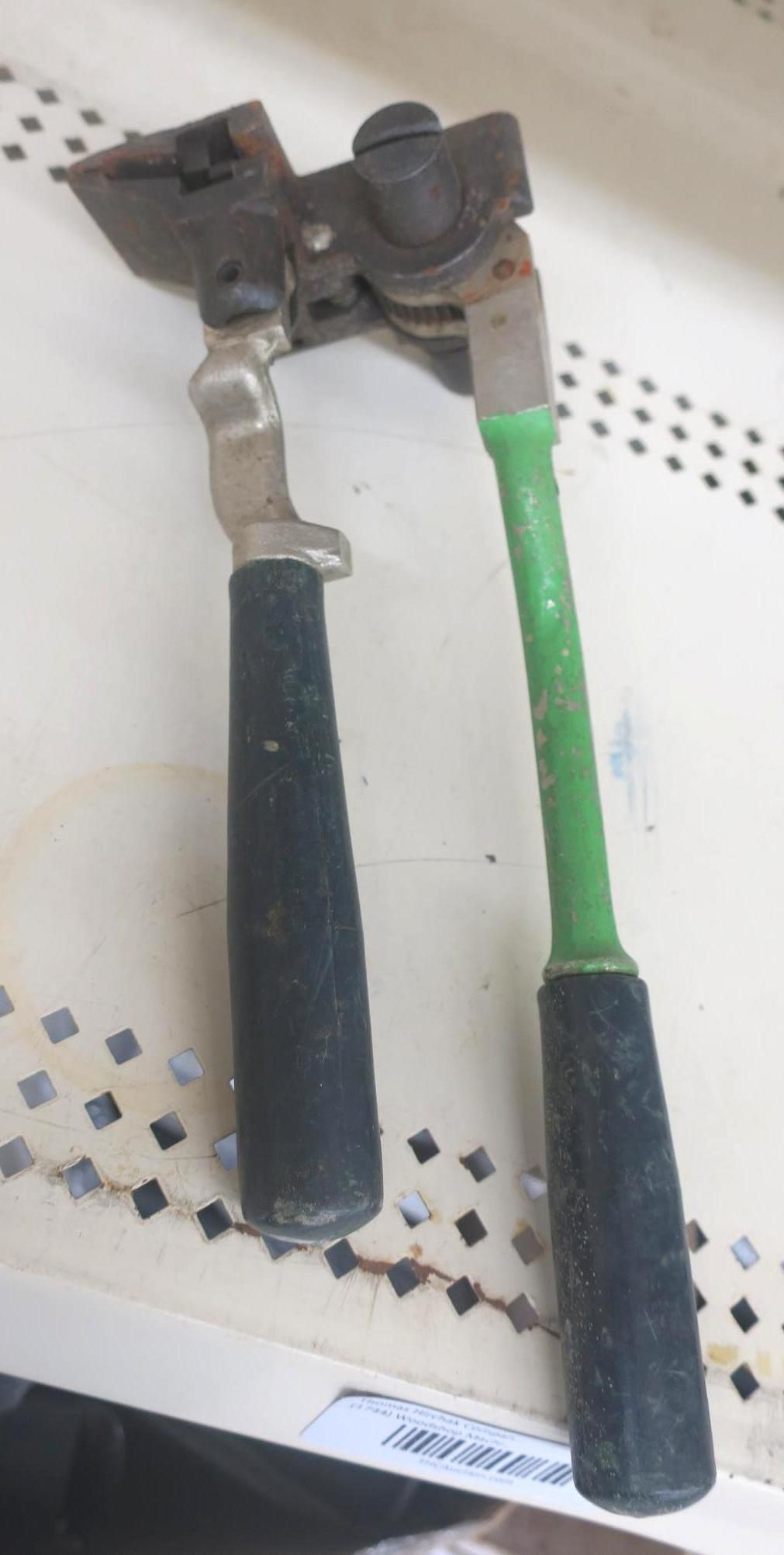 Two-handled bolt cutter with black and green grips on a light perforated surface