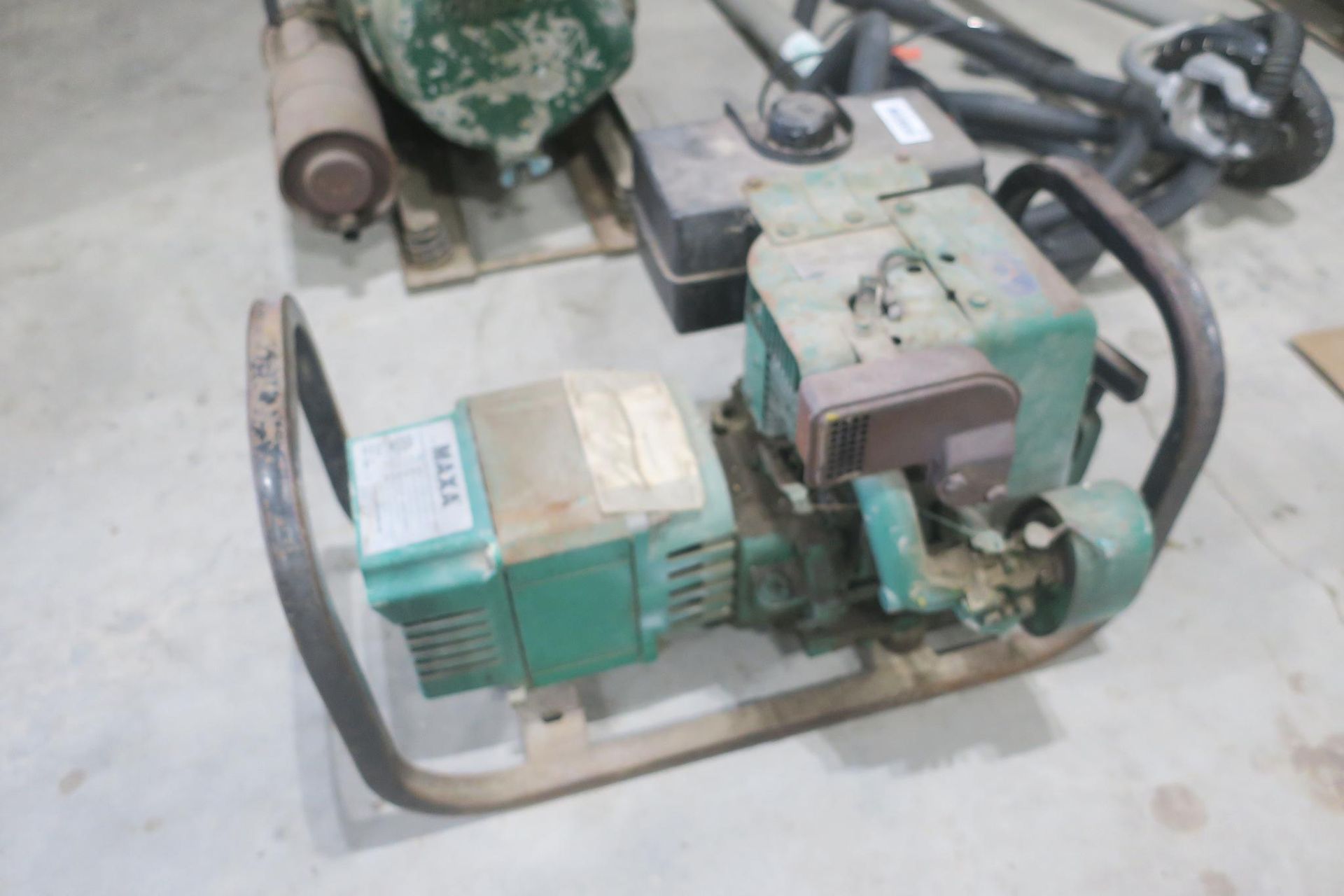 Small green industrial machine with a motor and hose on a concrete floor.