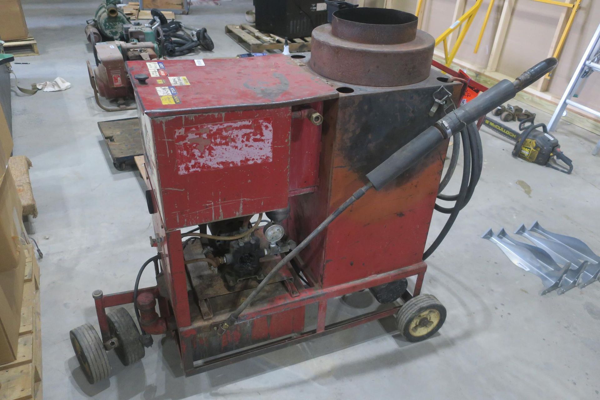 Red industrial machine with hoses and wheels in a workshop