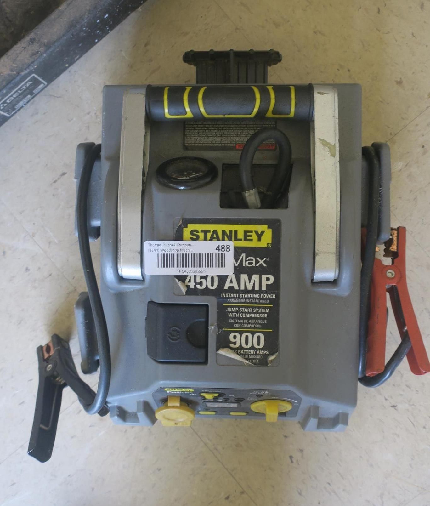 Stanley 450 AMP jump starter with red and black clamps on a beige floor.