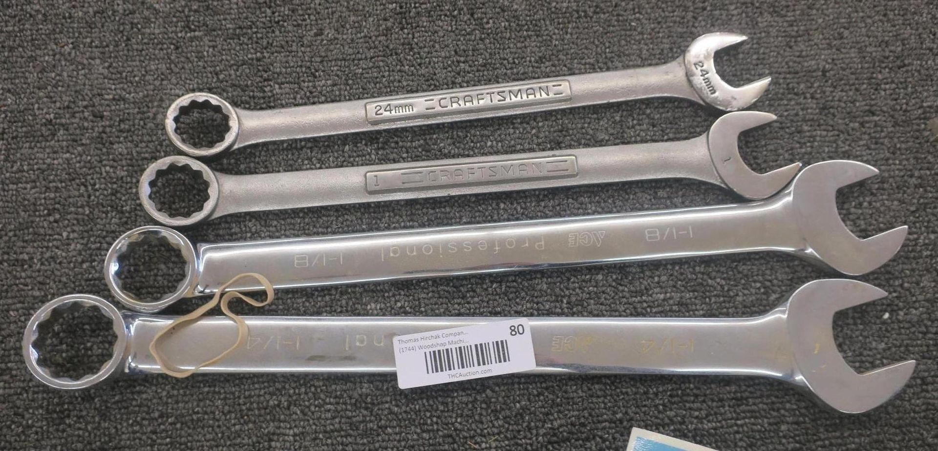 Four silver combination wrenches lined up on a textured gray surface.