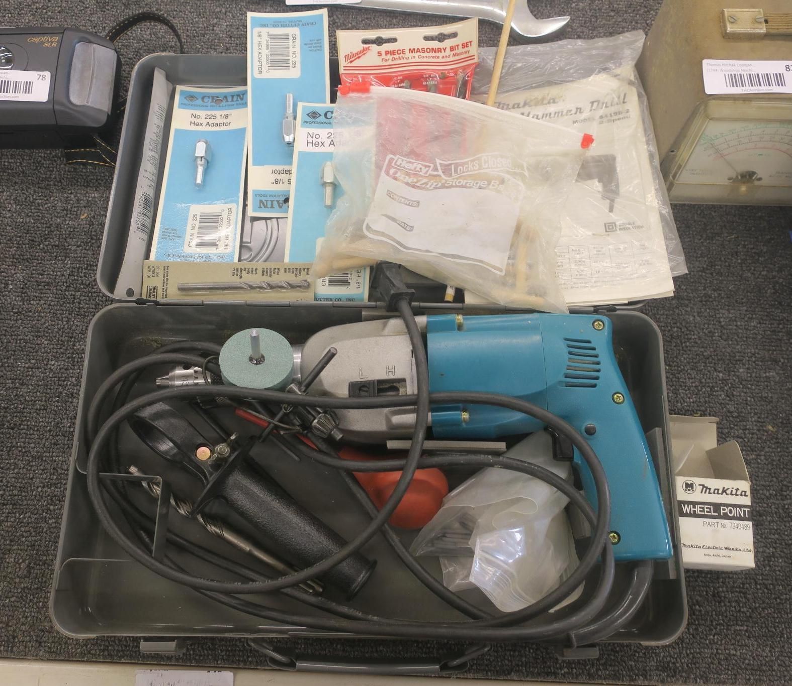 Tool case with a blue electric drill, coiled cords, and assorted small parts and supplies.