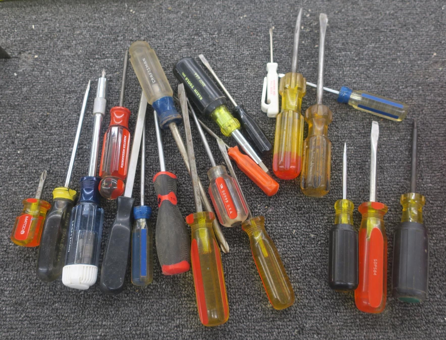 Assorted screwdrivers with clear, red, blue, and yellow handles spread on a gray surface