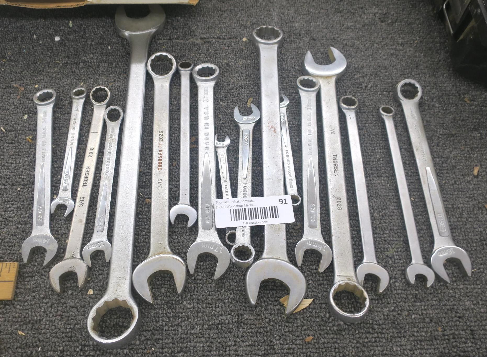 Assorted silver combination wrenches laid out on a dark carpeted floor, with a small label at center