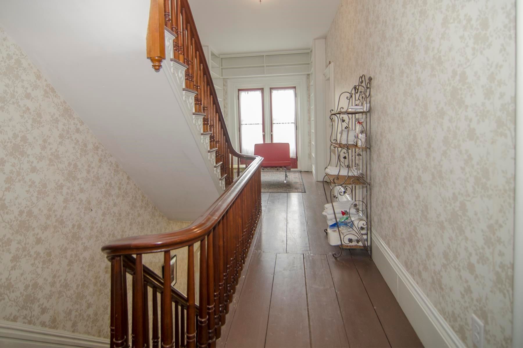 Wooden staircase and hallway with patterned wallpaper and an open door at the end.
