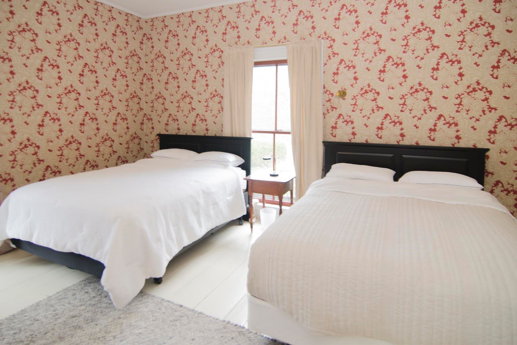 Bedroom with two beds, patterned wallpaper, window, and a small table.
