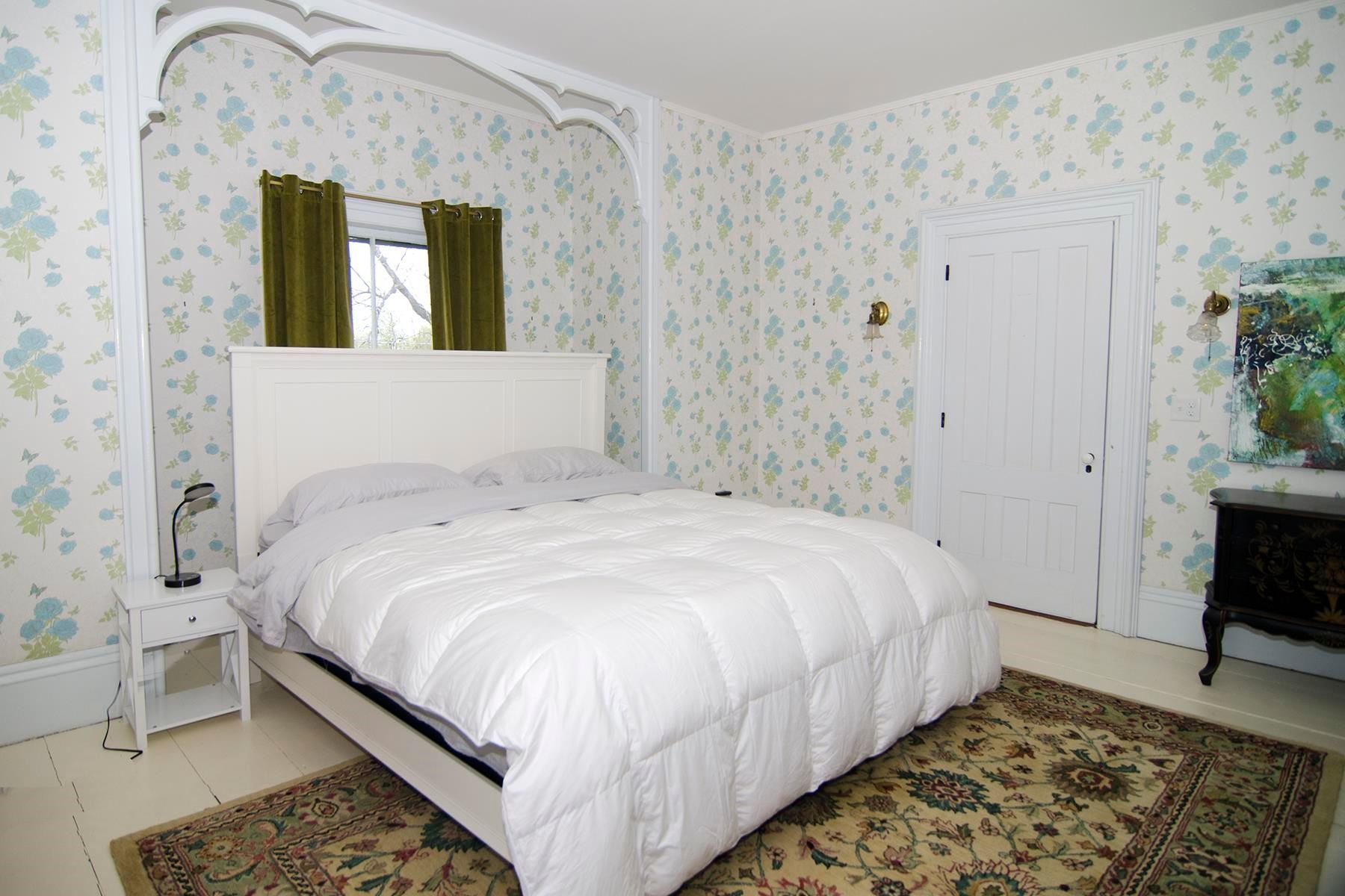 Bedroom with white bed, floral wallpaper, green curtains, and ornate white trim.
