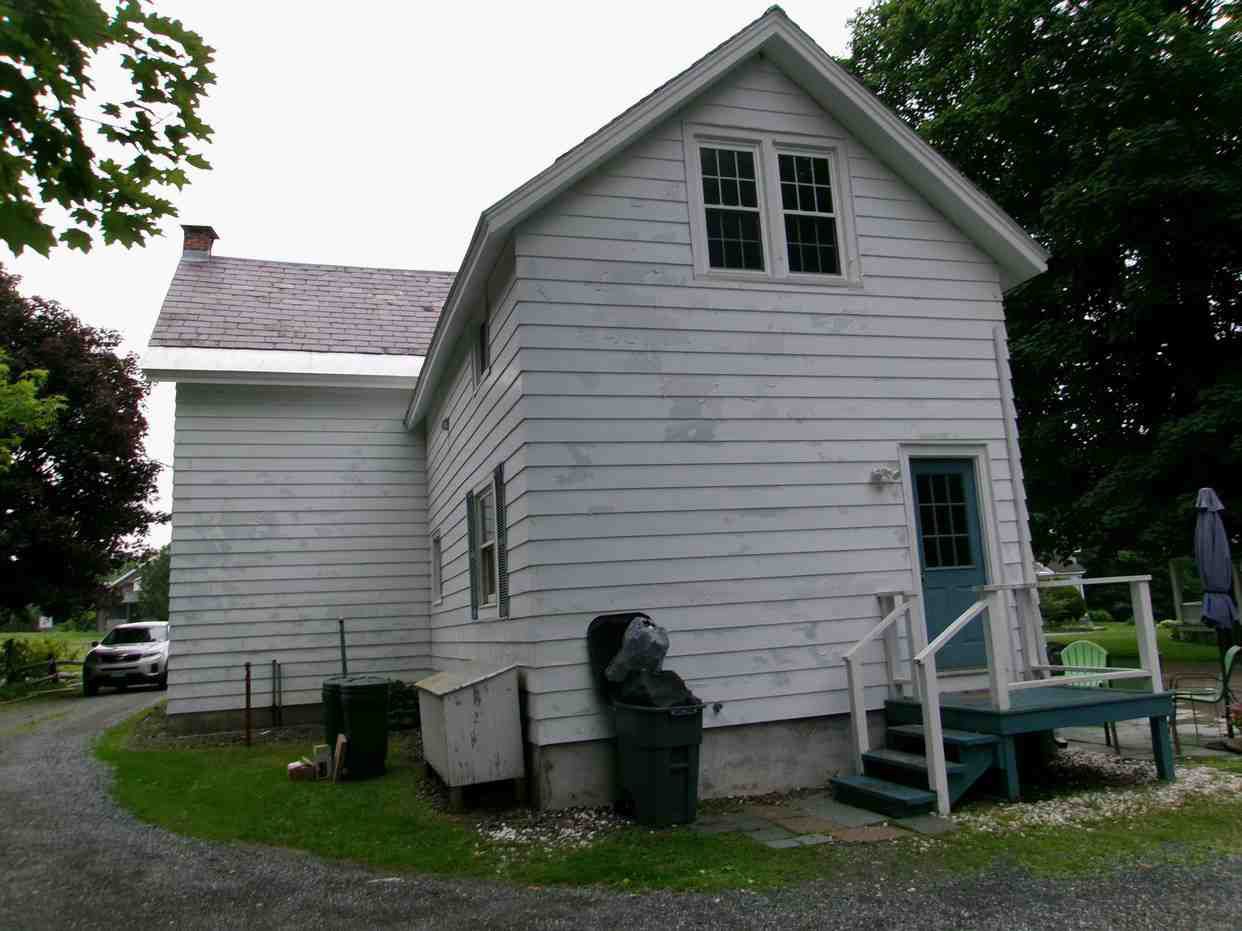 White house exterior with a small porch, side windows, and trash bins beside the wall.