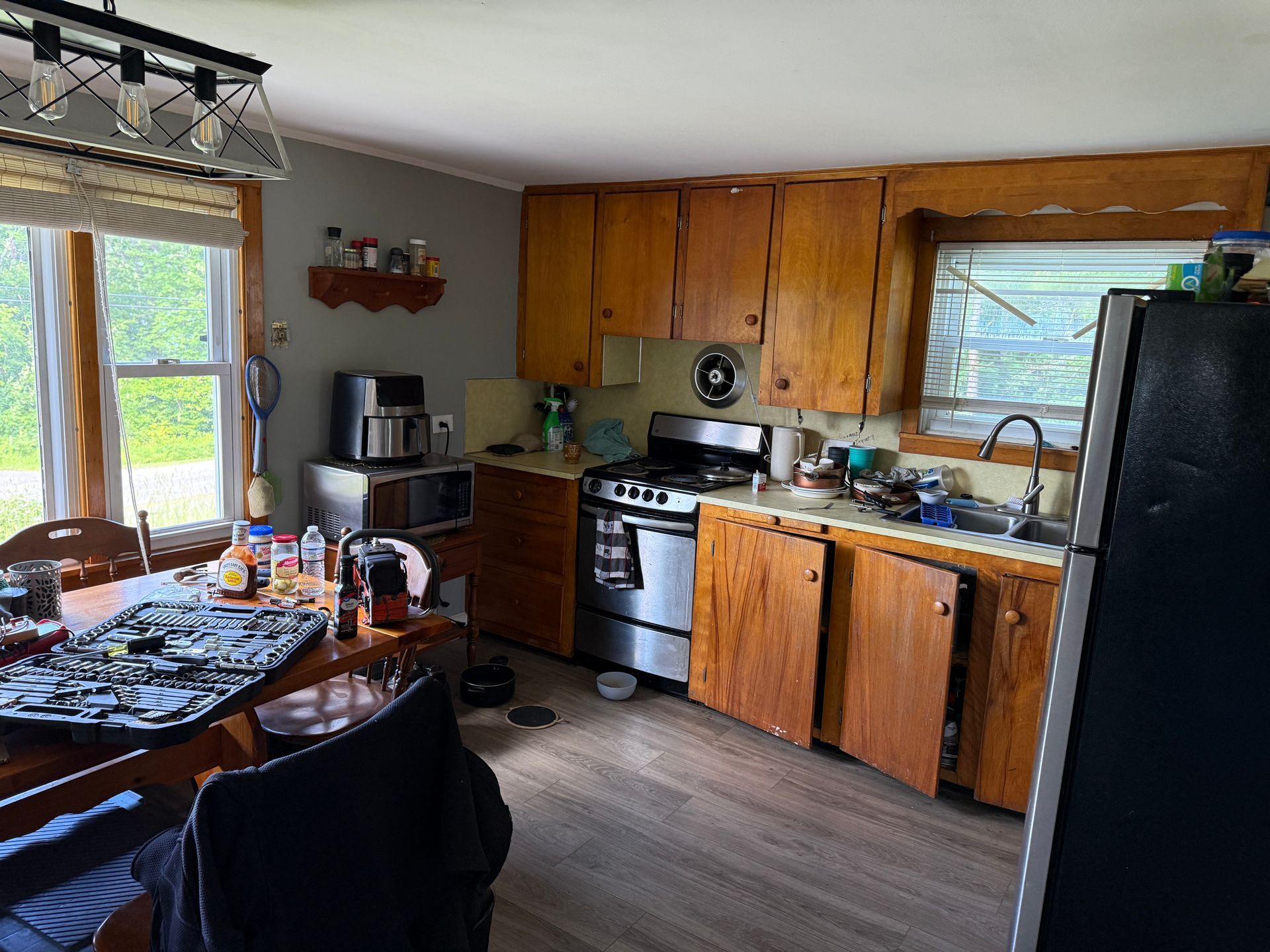 kitchen with wooden cabinets, black fridge, stove, sink, and dining table by a window.