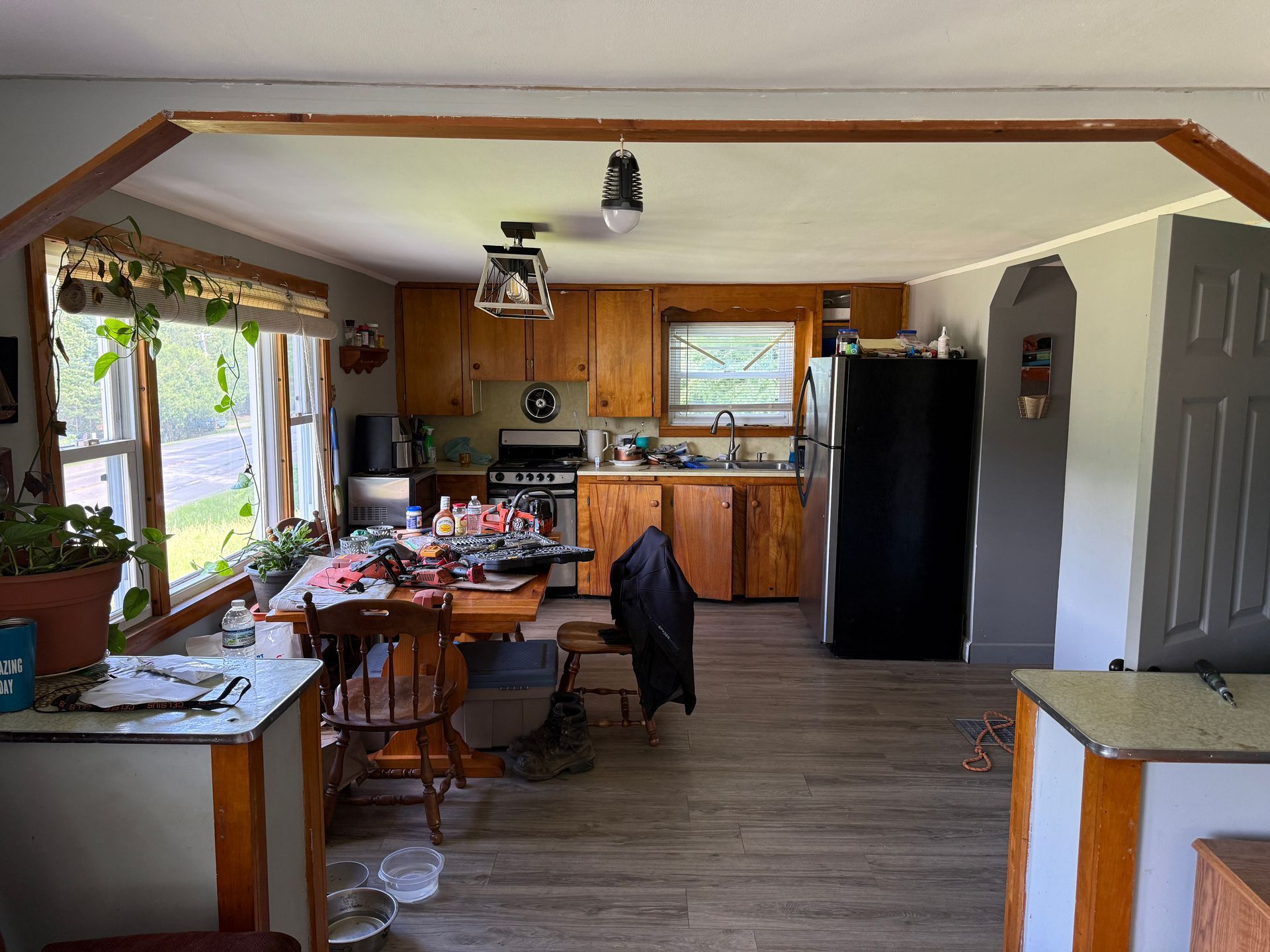 Kitchen and dining area with wooden cabinets, black refrigerator, and a table by a bright window.