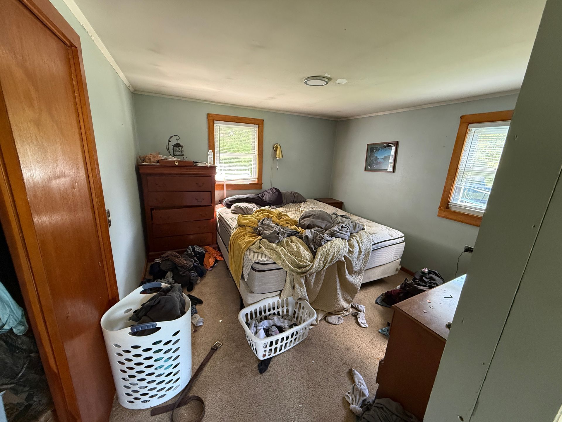 bedroom with bed, laundry baskets, dresser, and two windows with wood trim