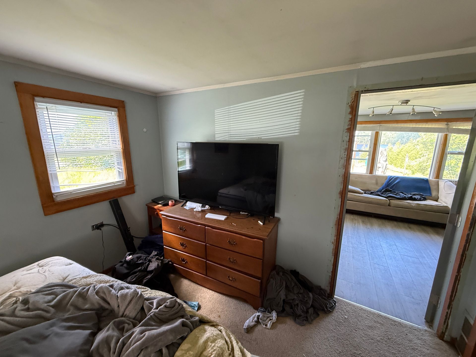 Small bedroom with a TV on a dresser, a bed, and a doorway to a sunlit room