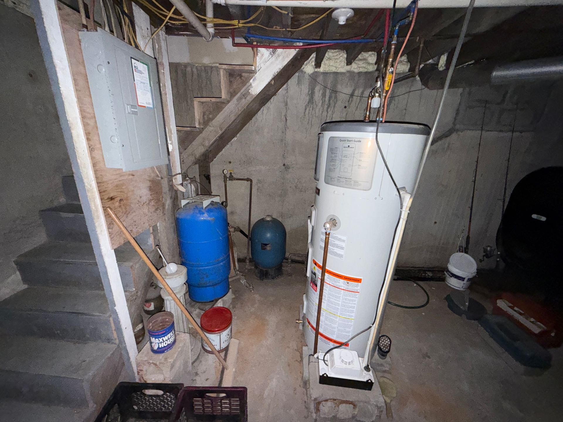 Basement utility room with water heater, blue tank, stairs, and exposed pipes.