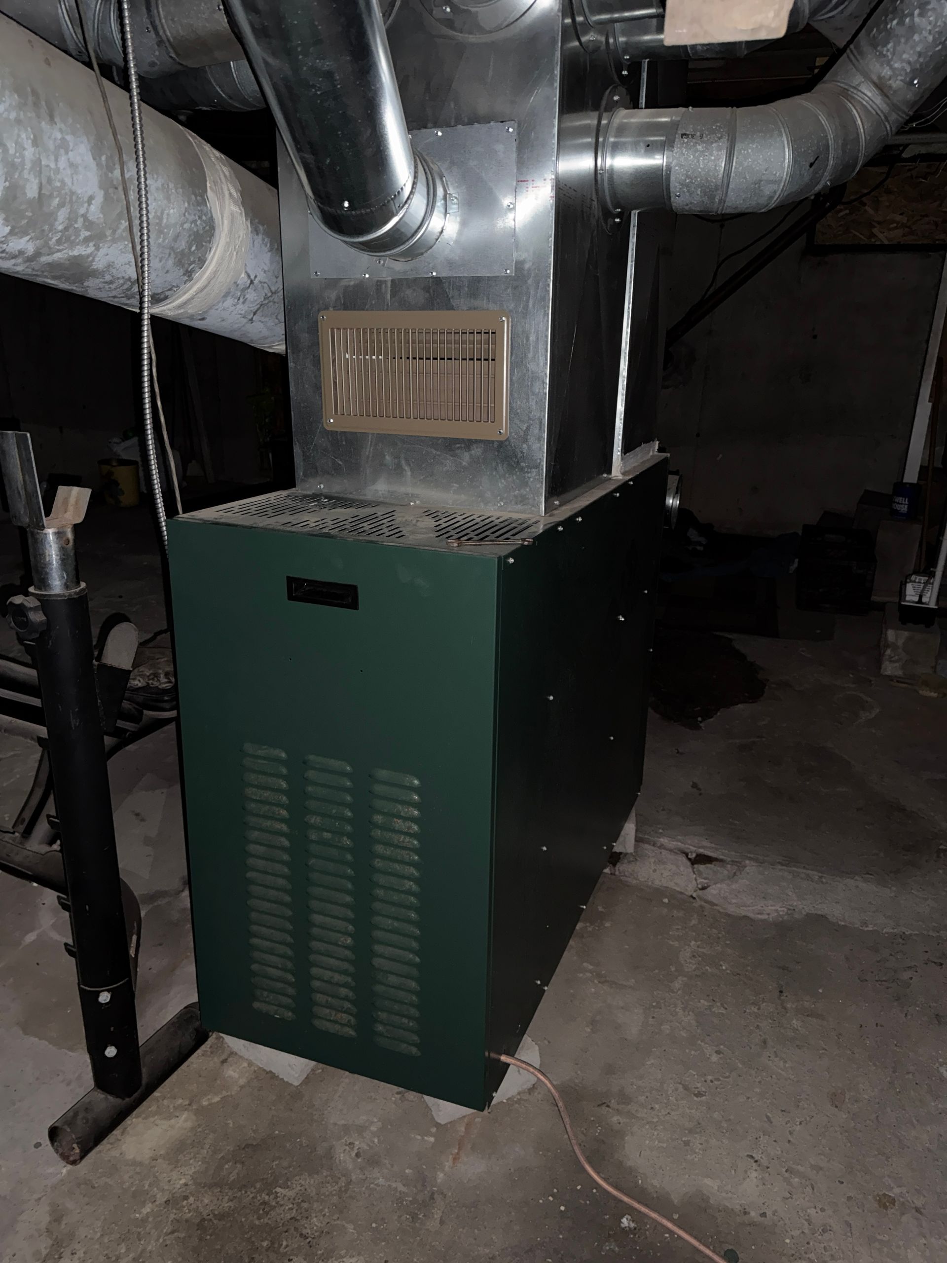 Green furnace with connected metal ducts in a basement utility area