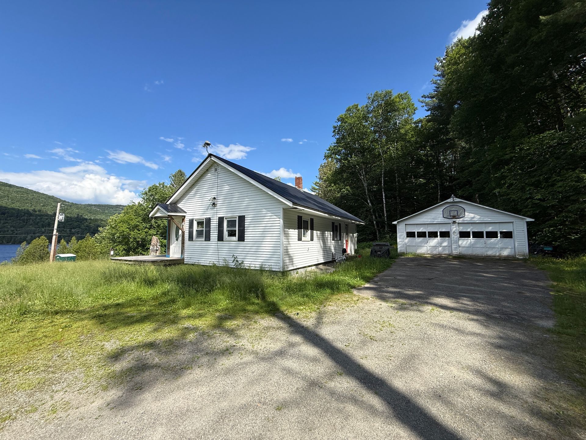 White house and detached garage on a gravel drive beside a grassy yard under a clear blue sky