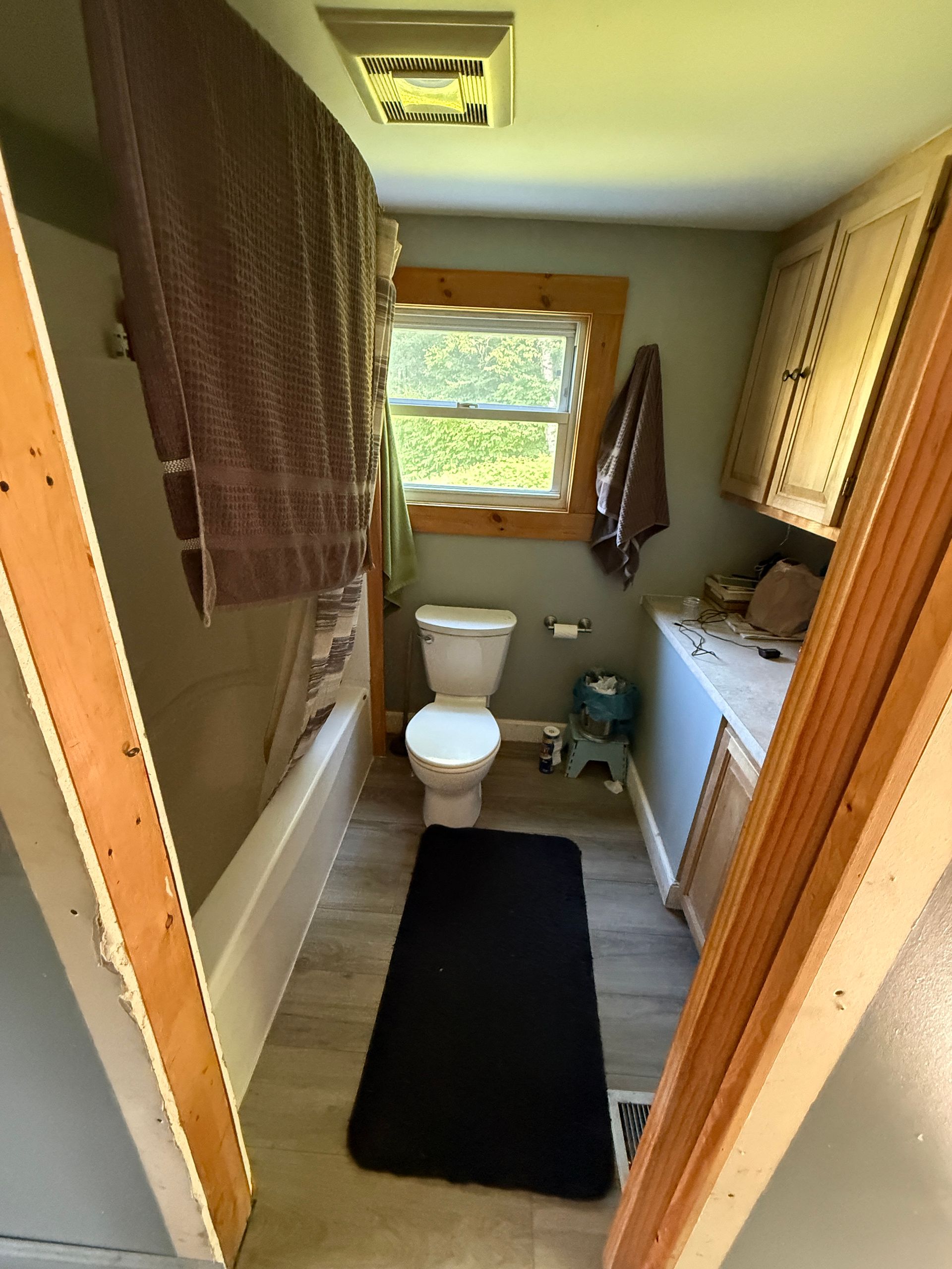 bathroom with bathtub, toilet, sink, window, and dark floor mat.
