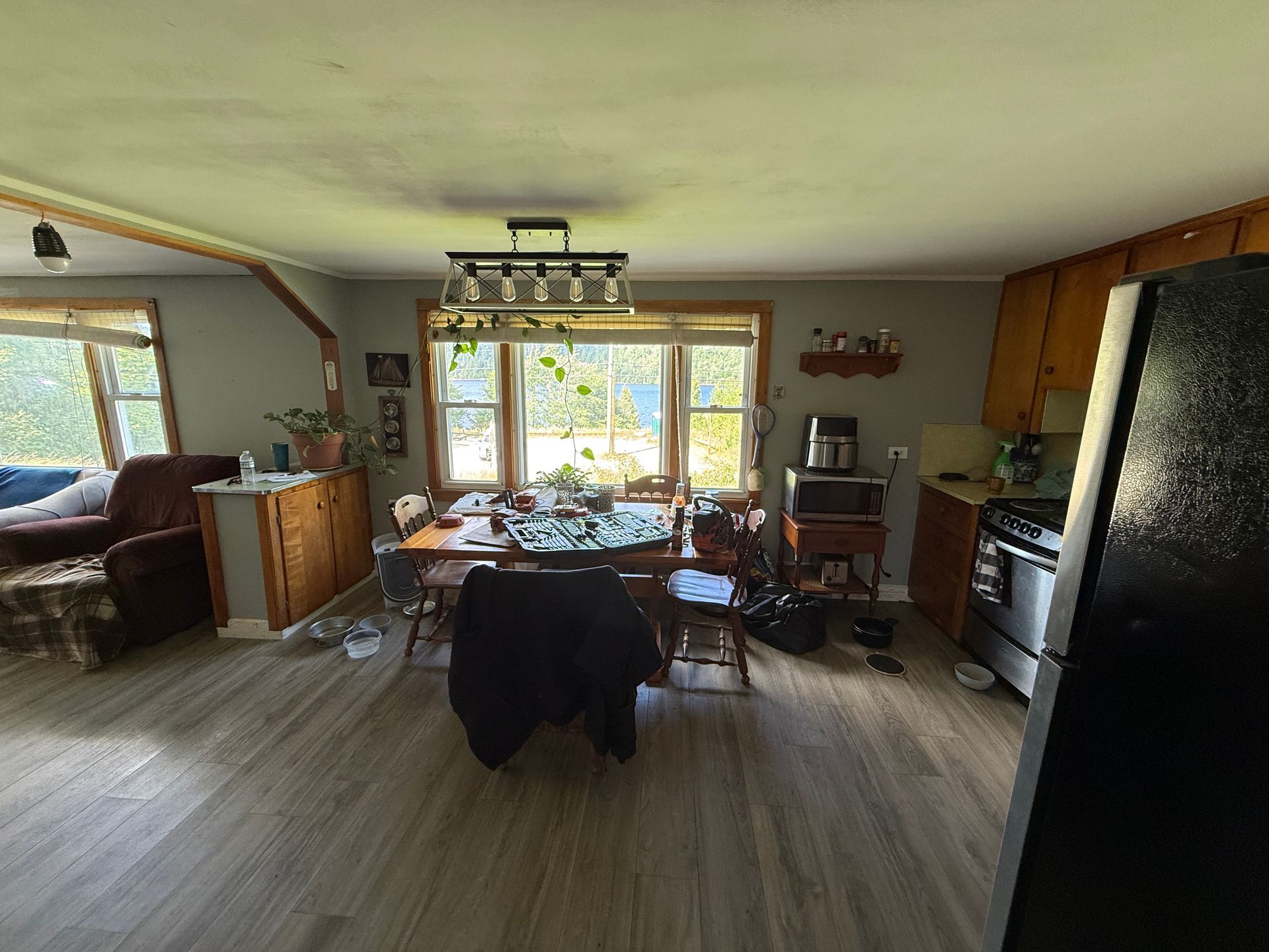 Cozy dining room with wooden table, large windows, and kitchen cabinets; sunlit interior with dark chairs.