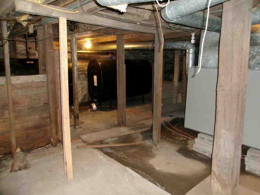 Crawl space under a house with exposed wooden beams, pipes, and a concrete floor.