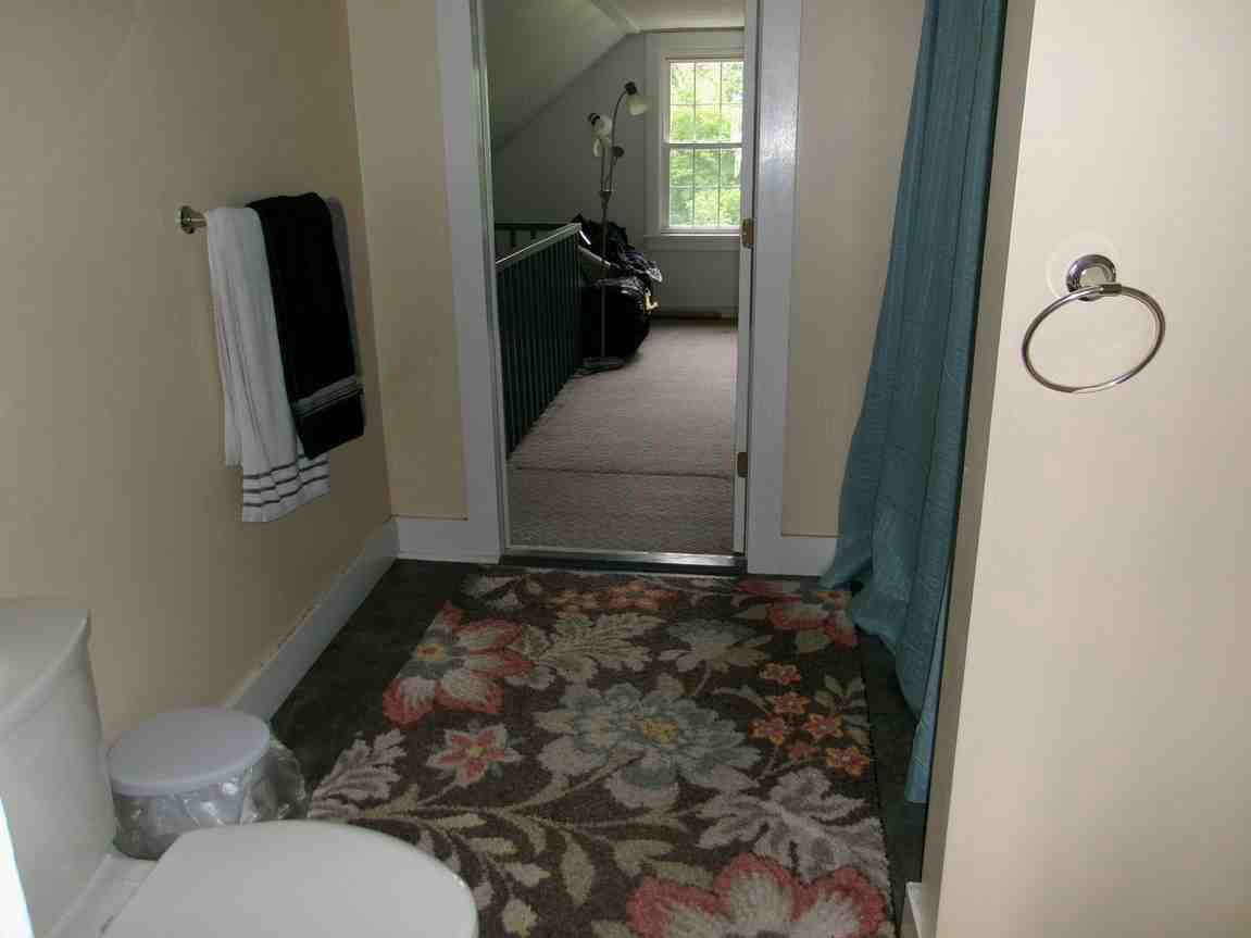 Bathroom with floral rug, towel rack, bathtub, and doorway to a bedroom with a bed and window.