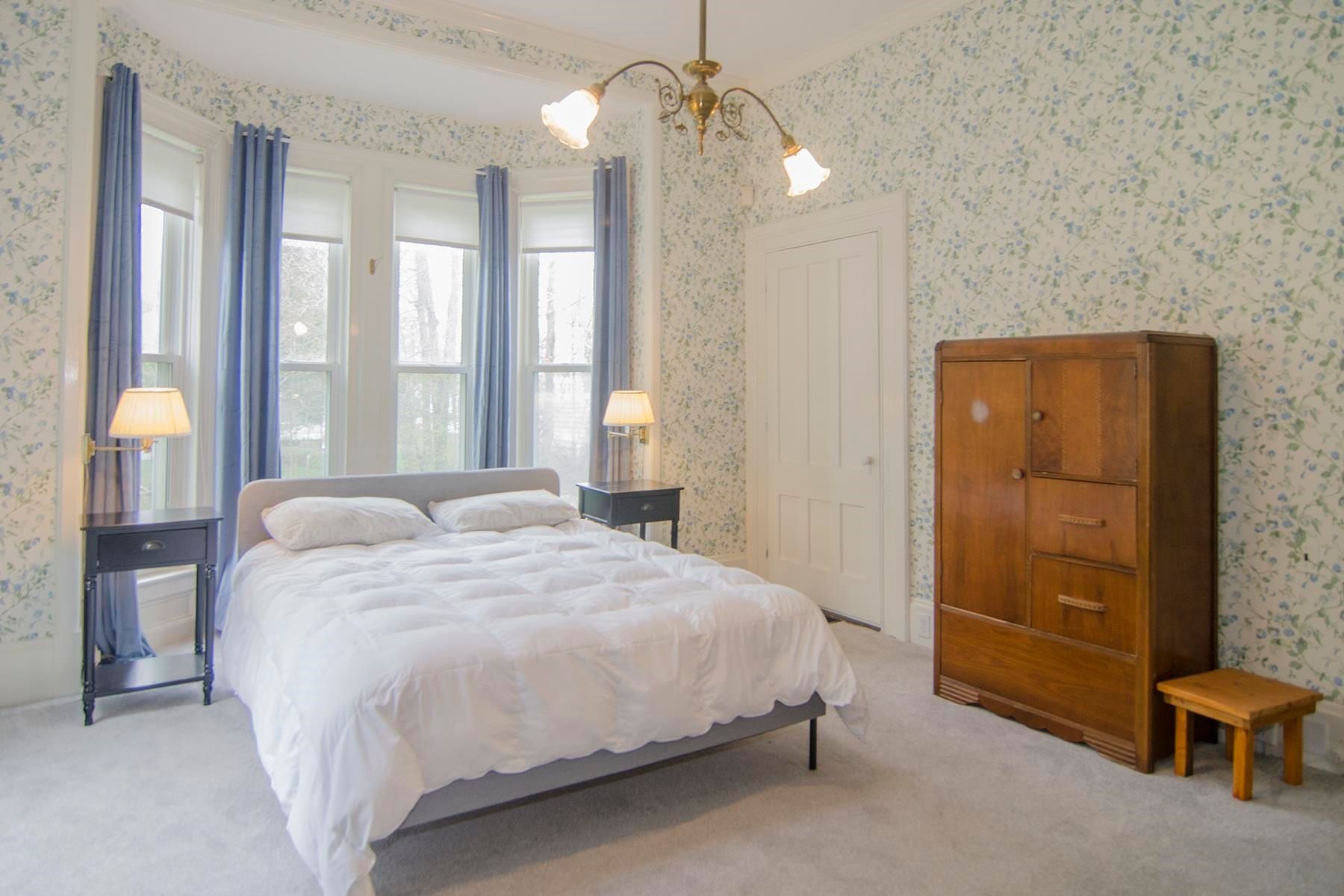 Bedroom with bed, nightstands, windows with blue curtains, wardrobe, and floral wallpaper.
