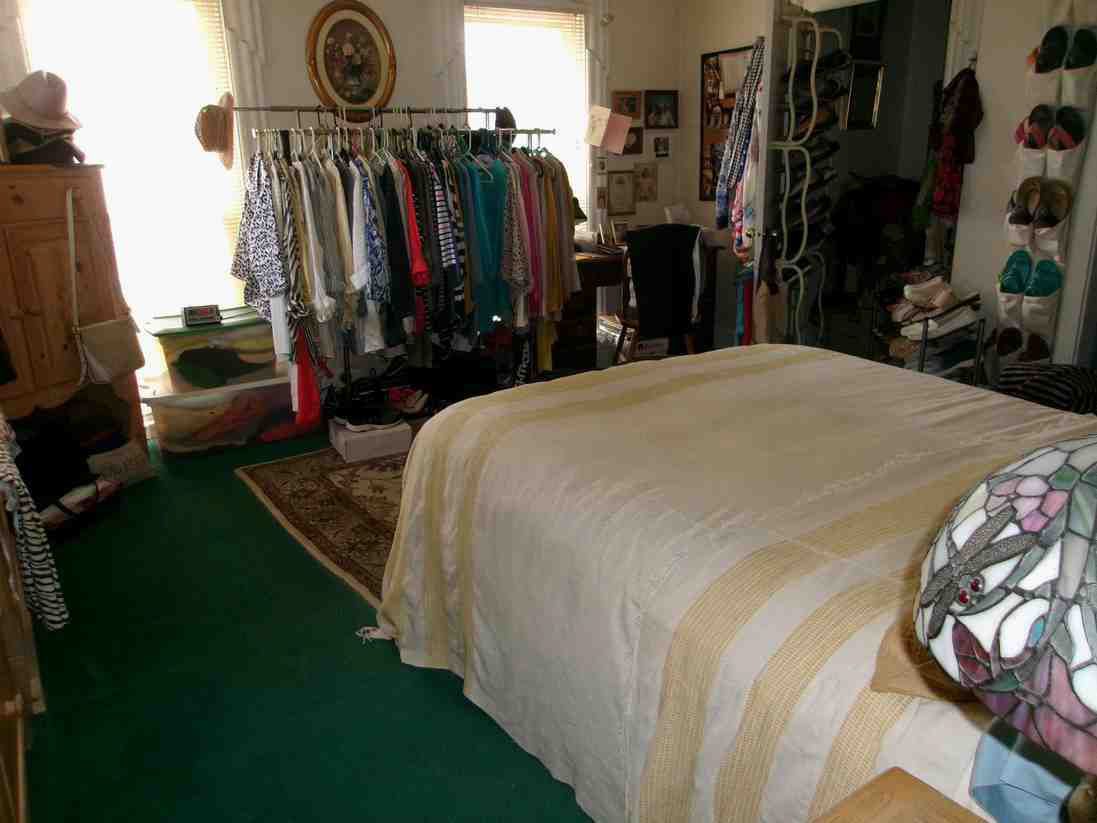 Bedroom with green carpet, bed, and clothing racks by a bright window
