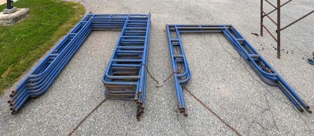 Blue metal frames and rails stacked on gravel outdoors, arranged in two piles