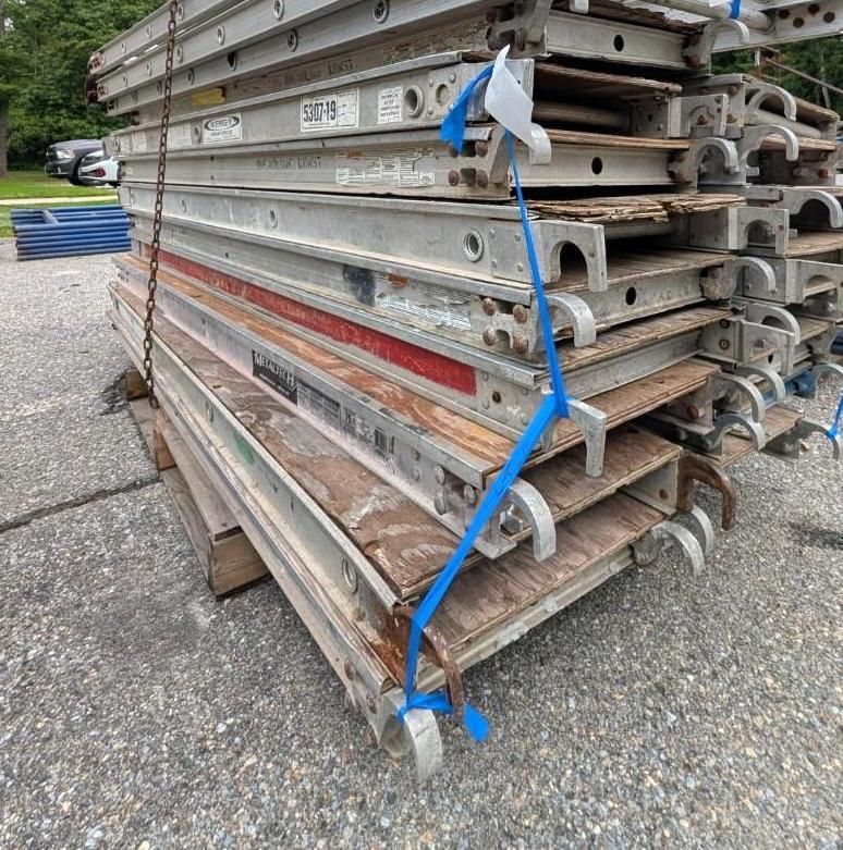 Stacked metal scaffolding planks strapped with blue banding on a pallet outdoors.