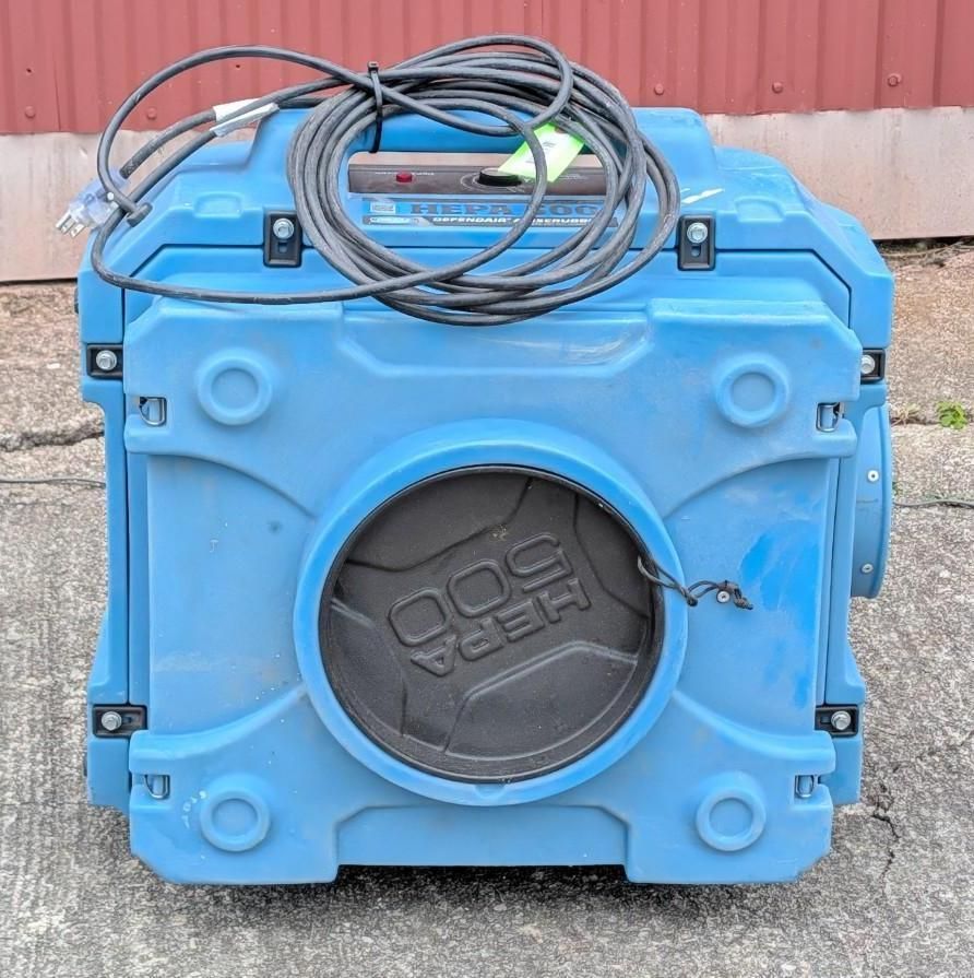 Blue portable industrial cleaning machine with coiled hose on top, shown against a red wall.
