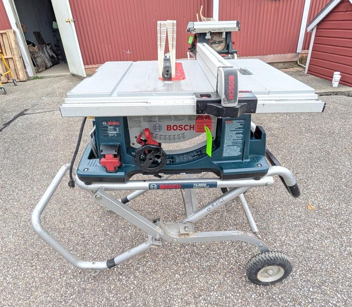 Bosch table saw on a wheeled stand outdoors on gravel near a red building