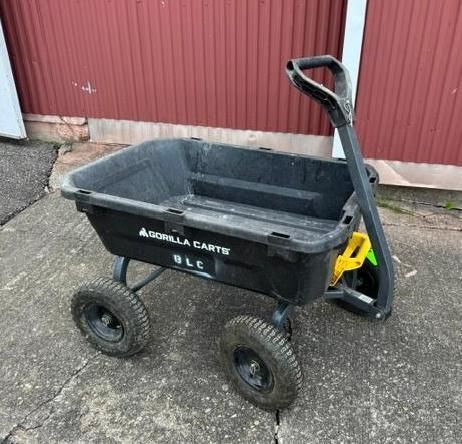 Black four-wheeled garden cart/dolly with handle on concrete beside a red wall
