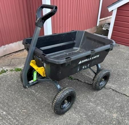 Black utility garden cart with four wheels and yellow handle on a concrete driveway