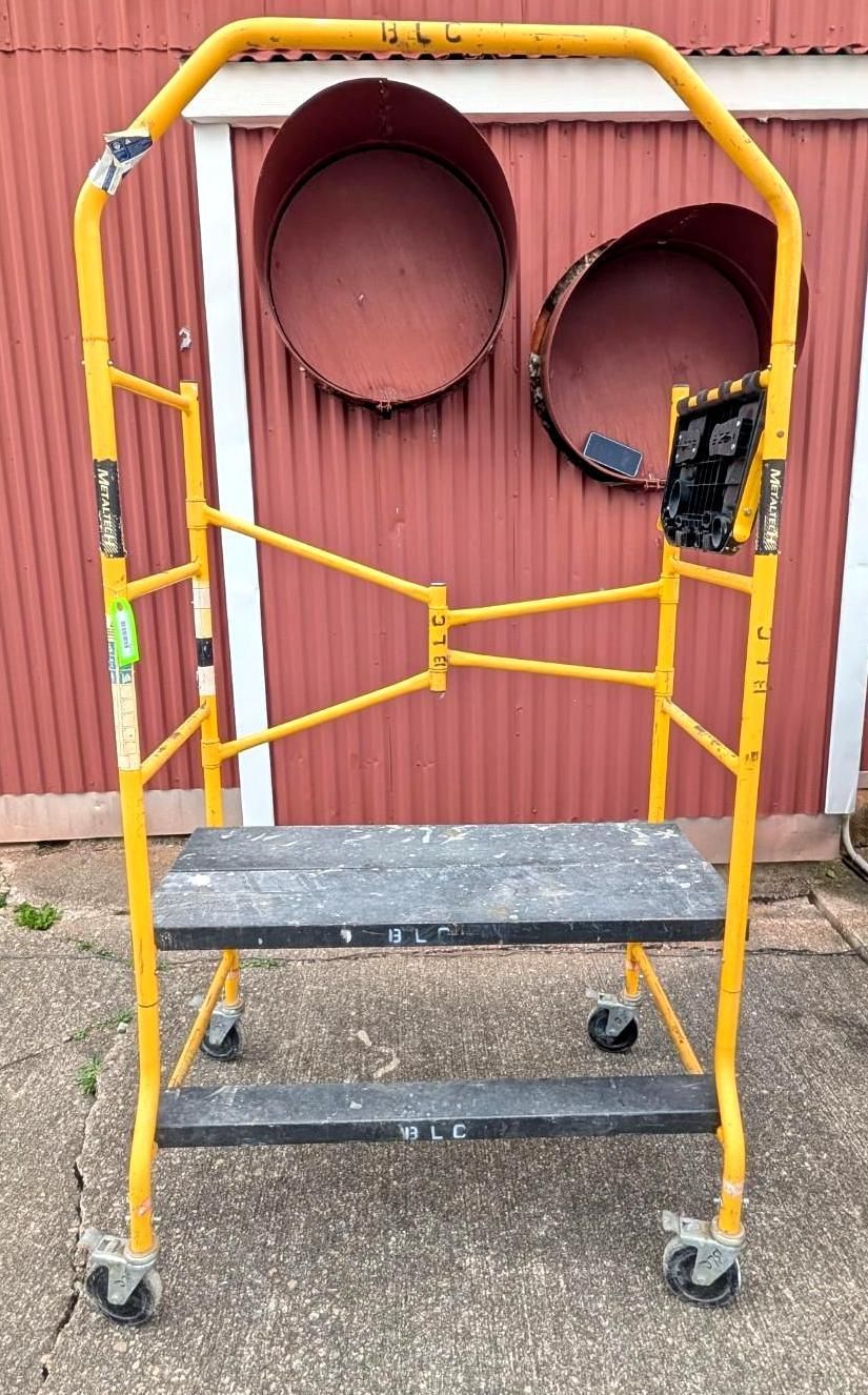 Yellow walker frame with wheels in front of a red corrugated wall and two round openings