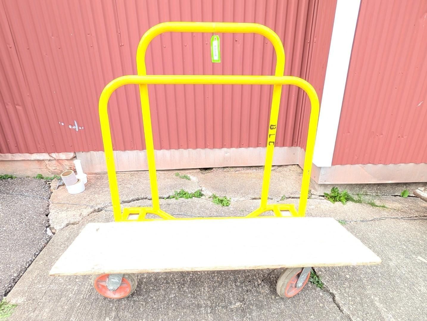 Yellow metal cart with white shelf and red wheels in front of a red wall.