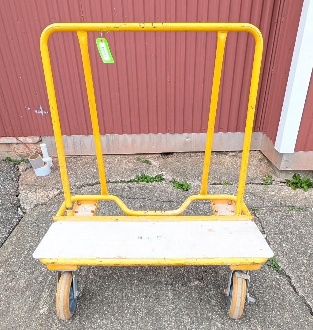 Yellow flatbed hand truck with white platform parked on pavement beside a red wall