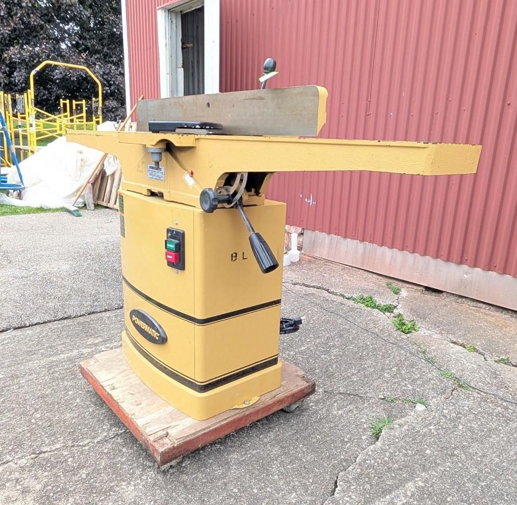 Yellow industrial lift platform on a wooden pallet beside a red metal building outdoors.
