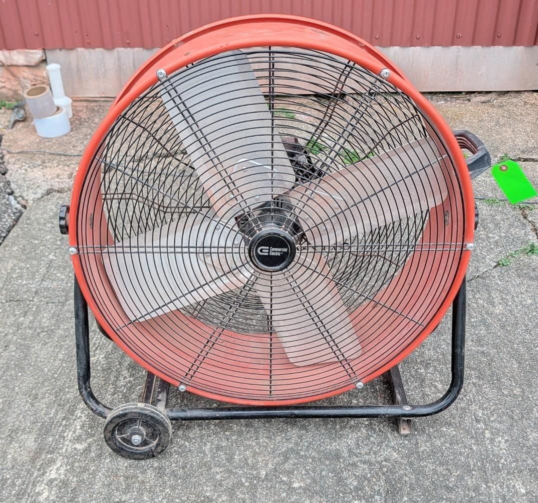 Large red industrial floor fan on a wheeled frame outdoors against a wall