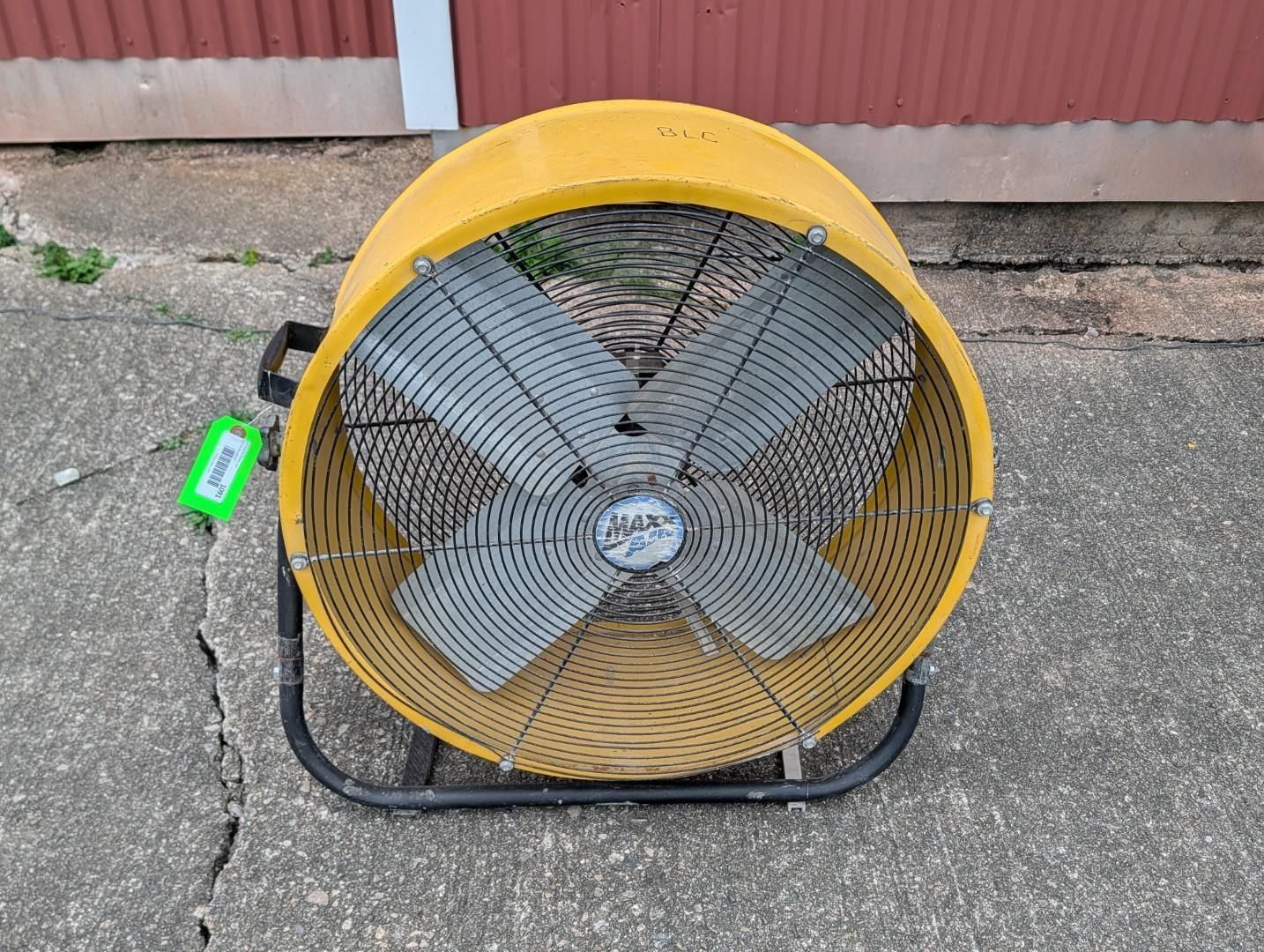 Large yellow floor fan on a concrete surface beside a red building wall.