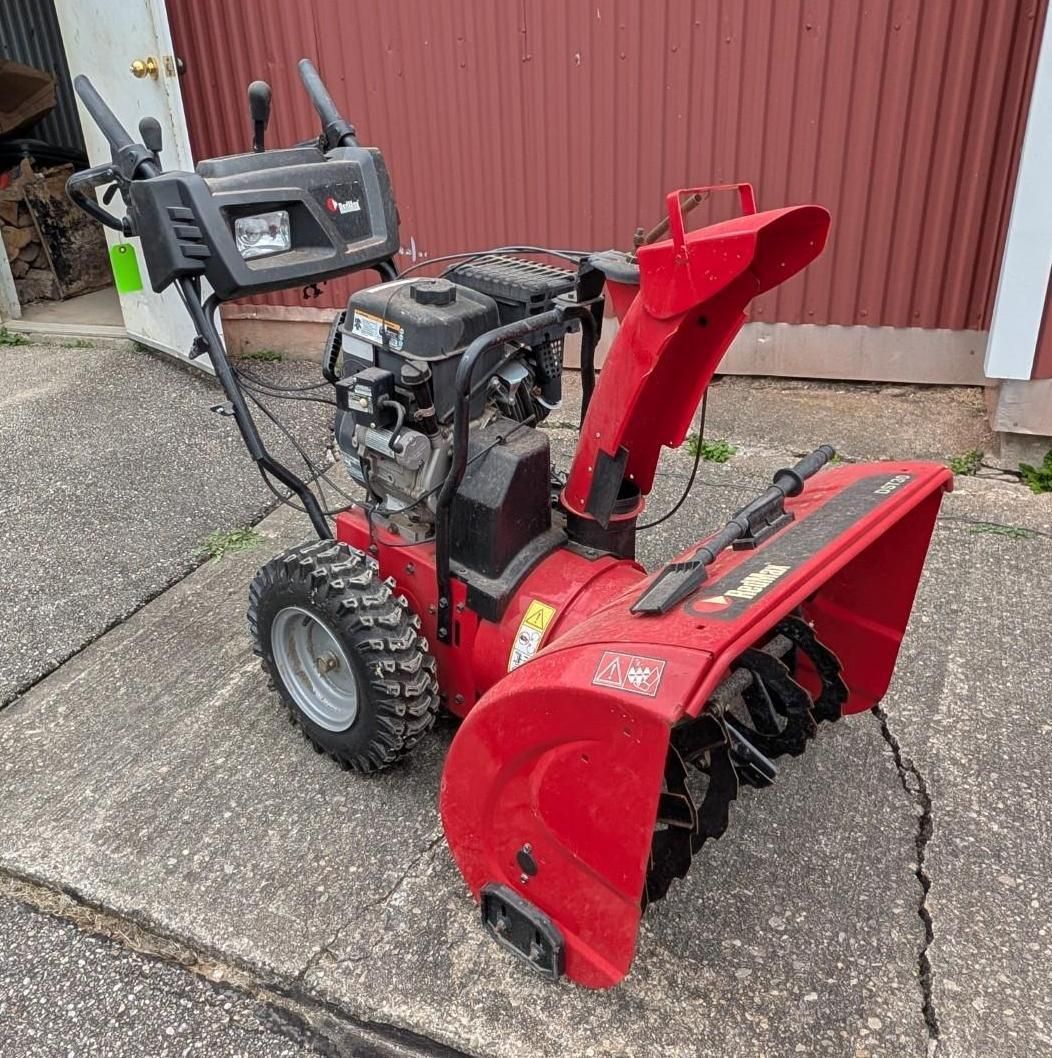 Red snow blower on a driveway beside a red garage wall