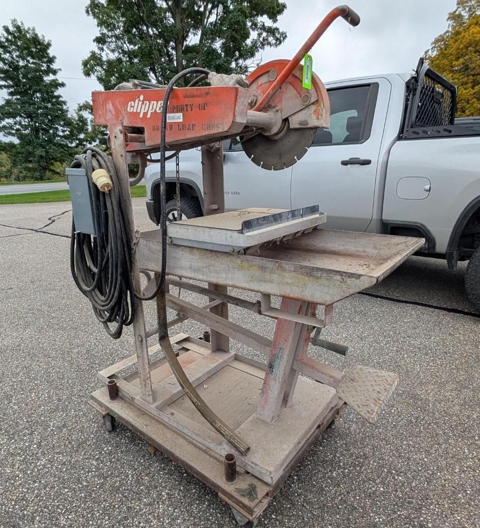 Orange concrete saw on a metal stand beside a silver pickup in a parking lot.