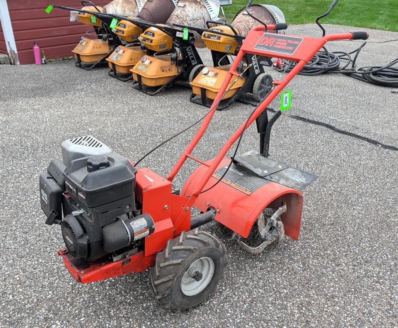 Red walk-behind tiller on gravel, with orange string trimmers stacked behind it.