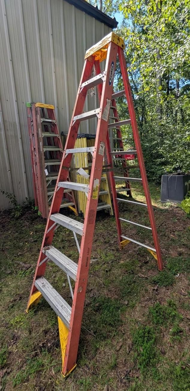 Two red step ladders leaning outdoors beside a shed and grassy yard