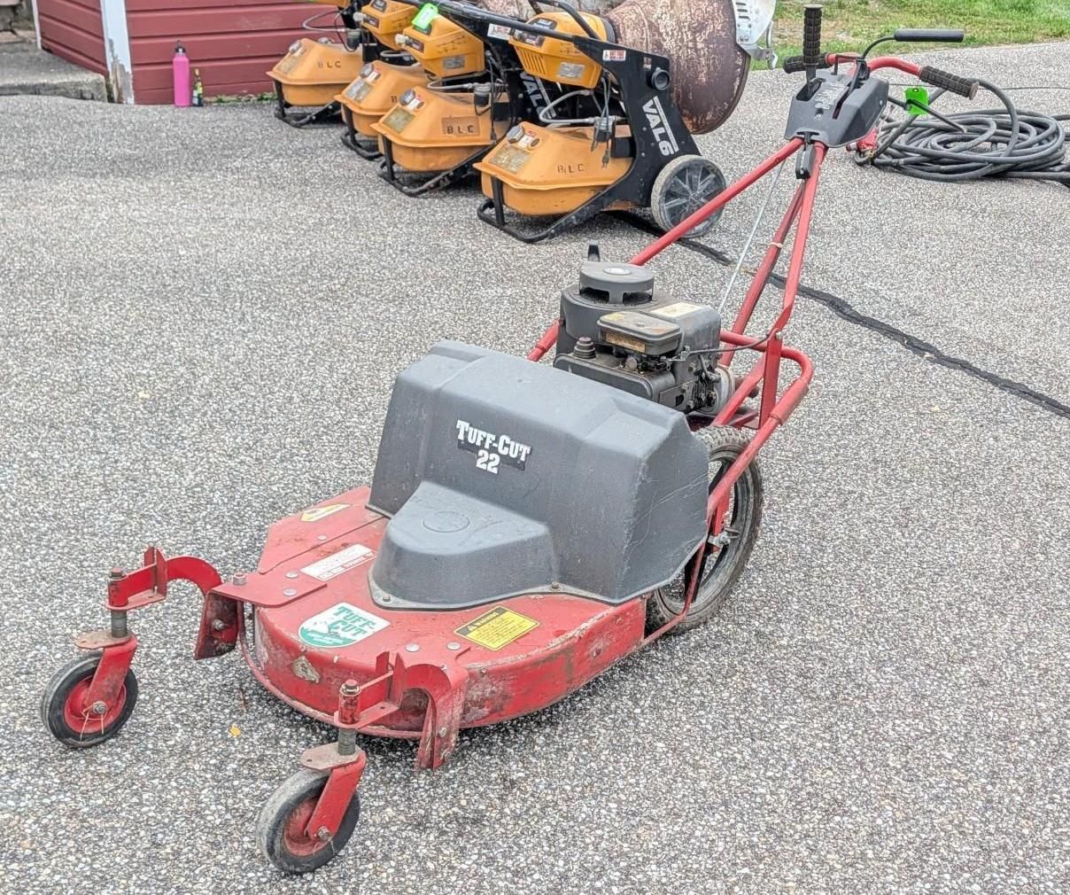 Red riding lawn mower parked on a gravel lot, with other mowers in the background.