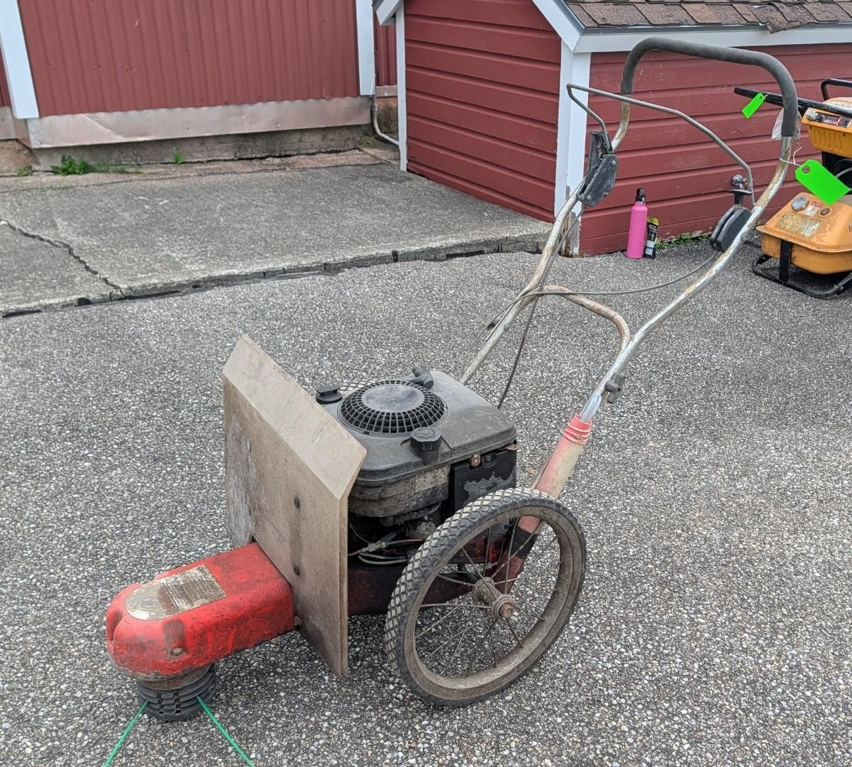 Homemade wheeled cart with motor and wooden panel on pavement beside red garage doors