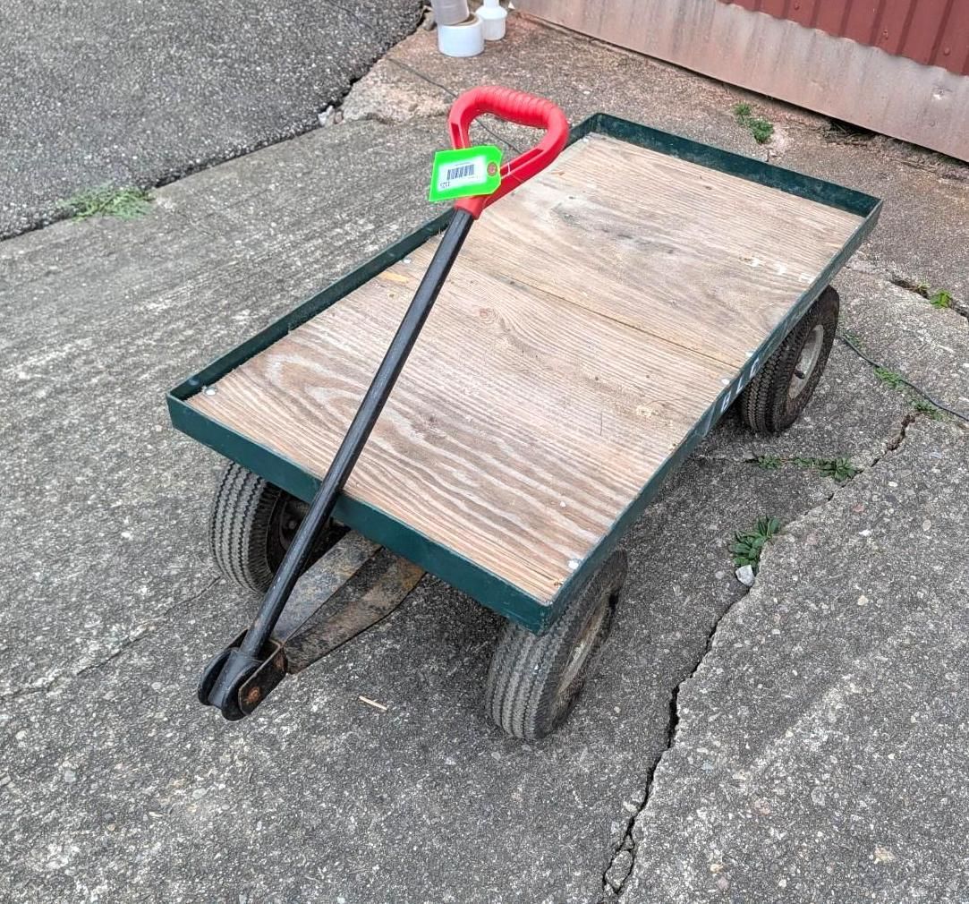 Wooden handcart with green frame, black wheels, and red handle on a paved surface.